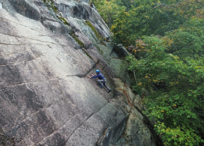 Person climbing a granite rock wall surrounded by trees.