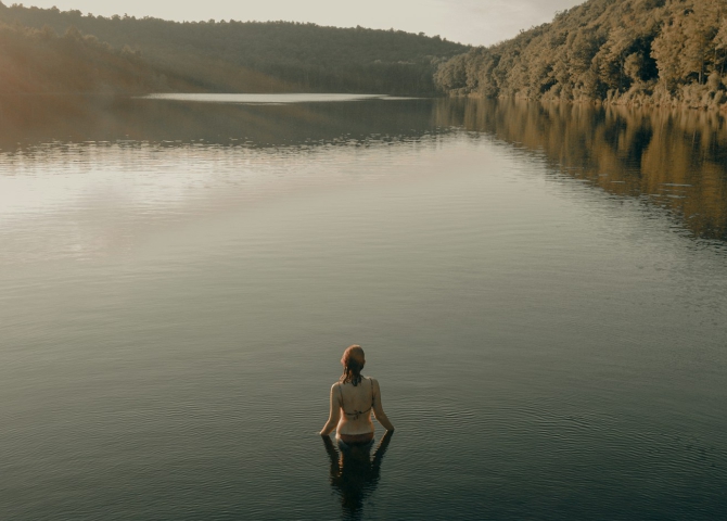 Woman swimming alone in a calm lake at sunset.